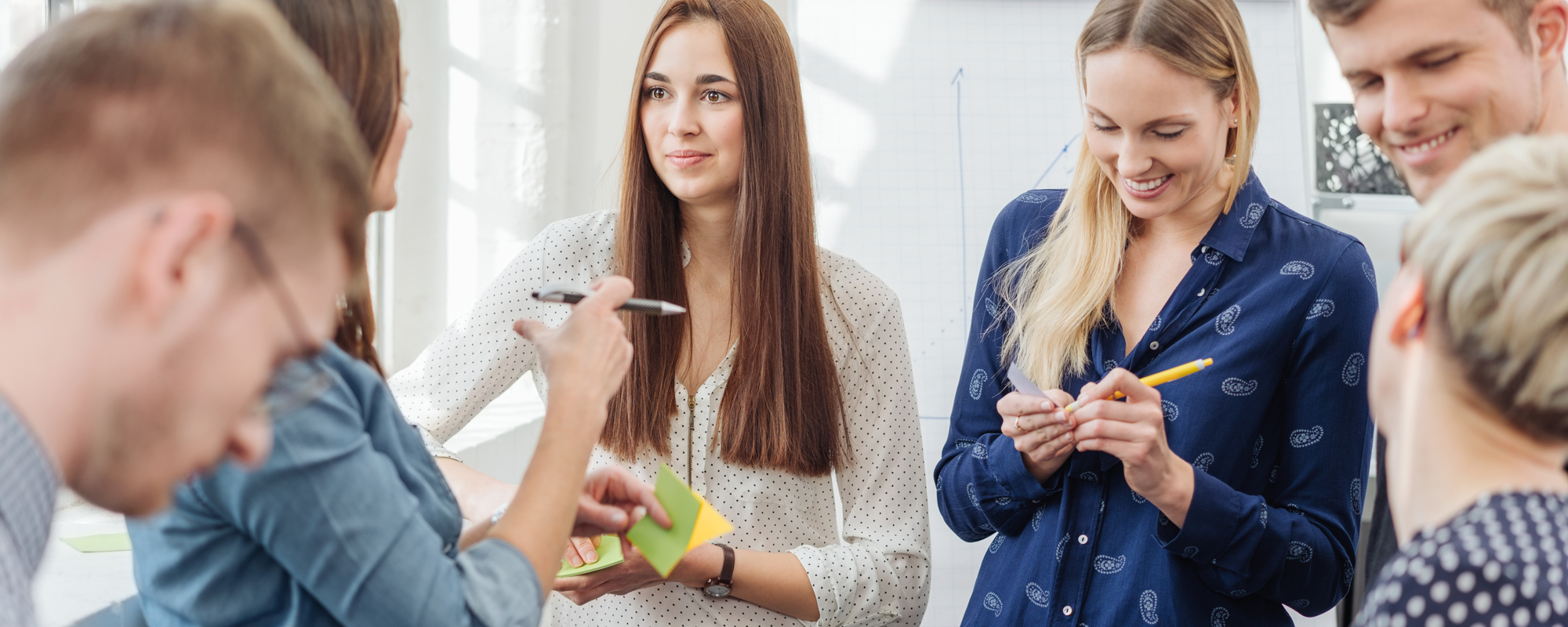 Networking im Beruf: 4 Frauen und 2 Männer stehen im Kreis, unterhalten sich und machen Notizen auf bunten Post-its