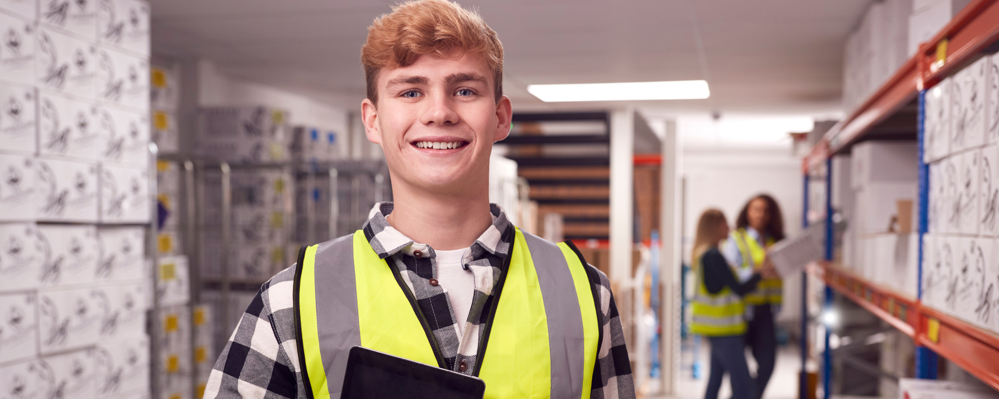 Teenager mit gelber Arbeitsweste steht grinsend in einem Warenhaus