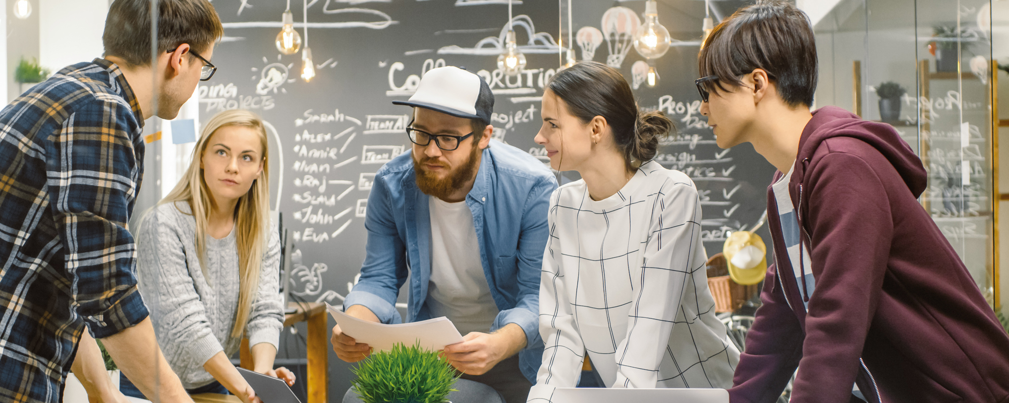 Start-up gründen: Junges Team steht um einen Tisch in einem modernen Büro mit geöffneten Laptops und mehreren Unterlagen.